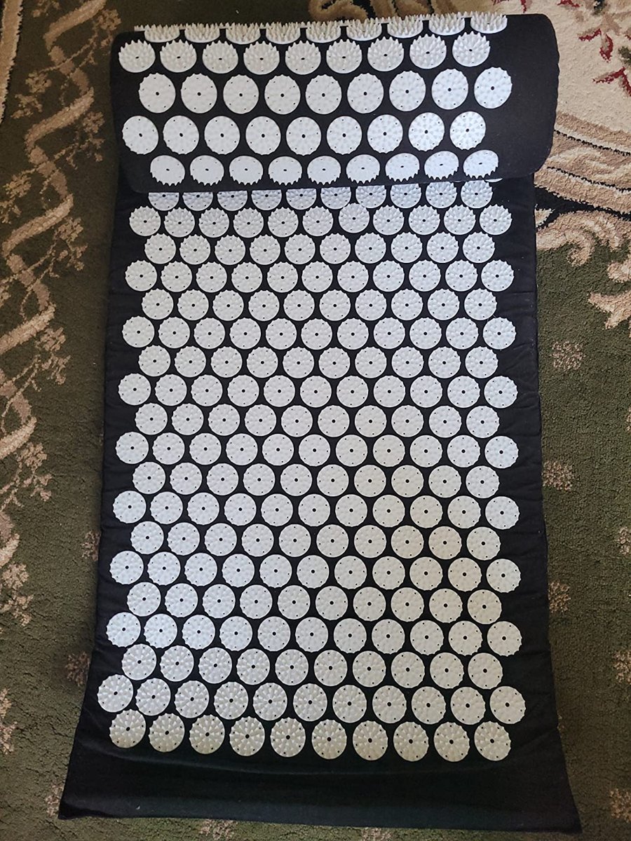 Top-down customer photo of the full acupressure mat and pillow unrolled on a rug